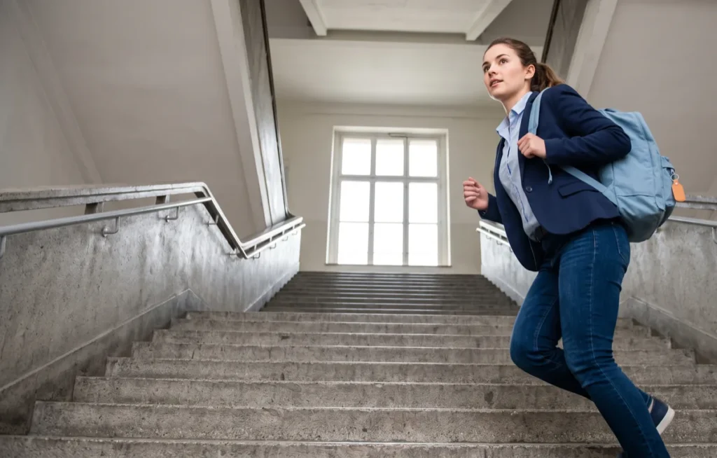 Studentka wbiega po schodach budynku uczelni z plecakiem na ramieniu